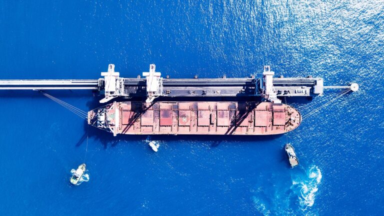 Varios remolcadores ayudan en el atraque de un buque granelero en un muelle de descarga.